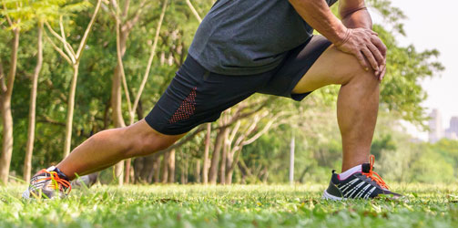 Man stretching knee in park